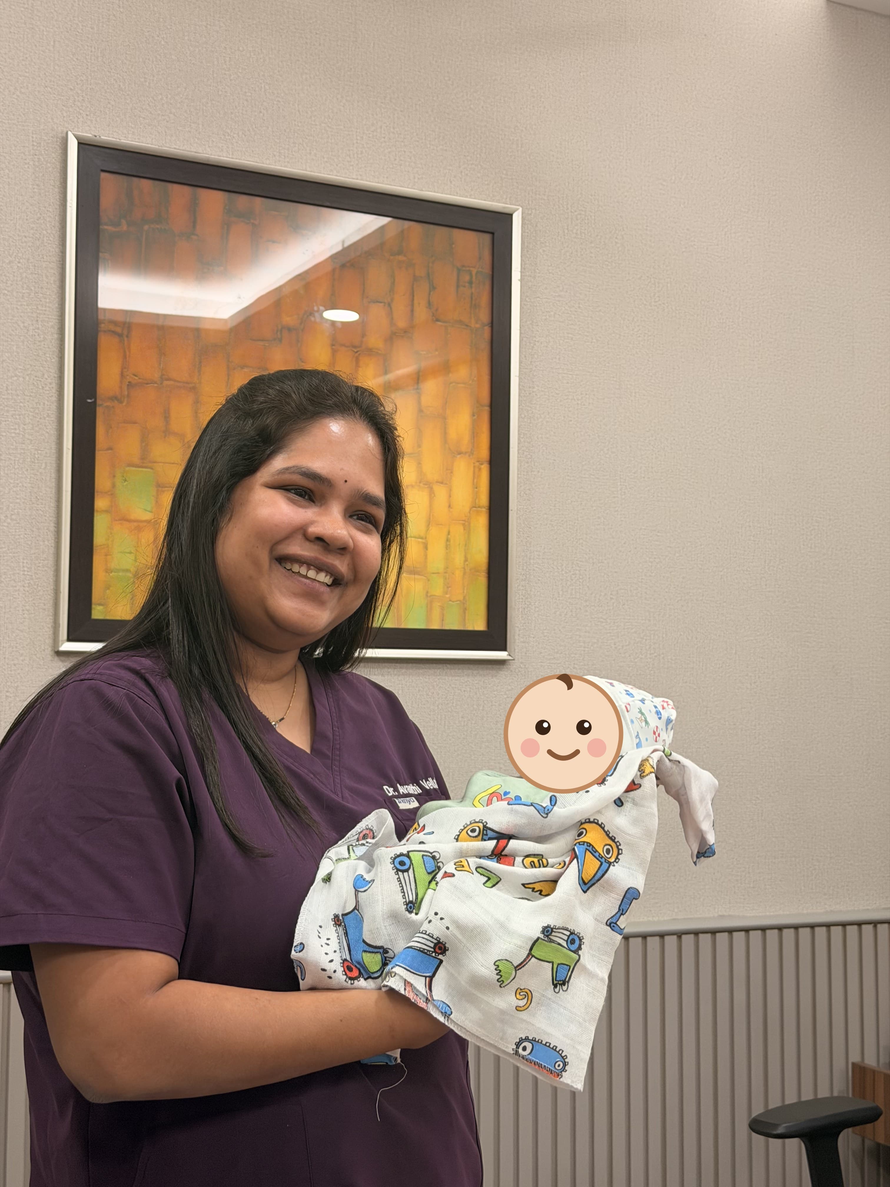 Dr. Vellala in scrubs holding a swaddled newborn