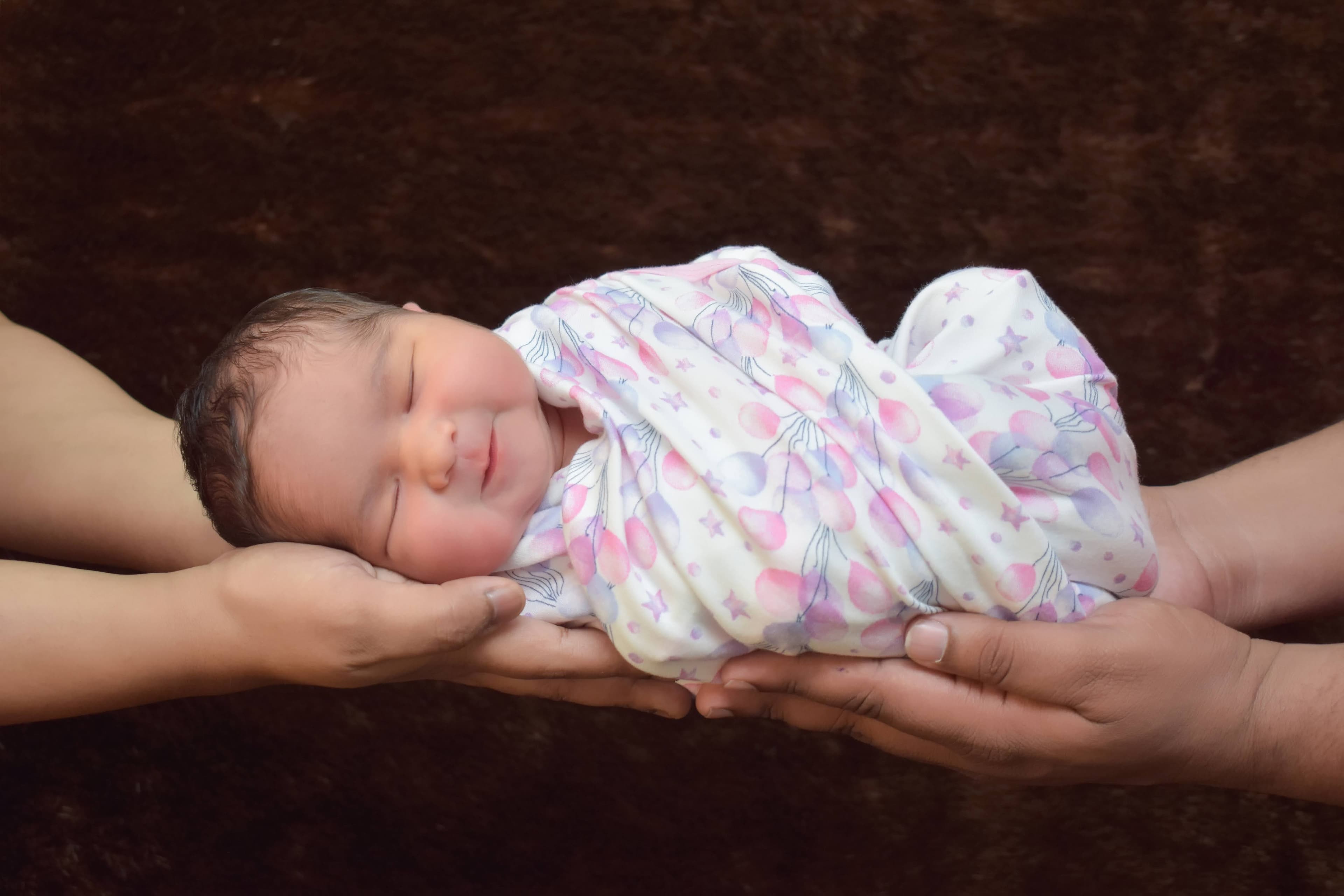 A newborn resting in her parents' cupped hands